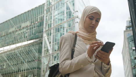 Muslimische-Geschäftsfrau-überprüft-Nachrichten-Auf-Dem-Mobiltelefon,-Während-Sie-Vor-Dem-Büro-In-Der-Stadt-Steht